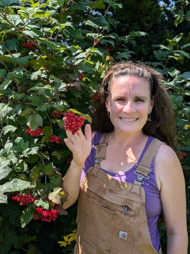 A woman standing in front of a bush with red berries.