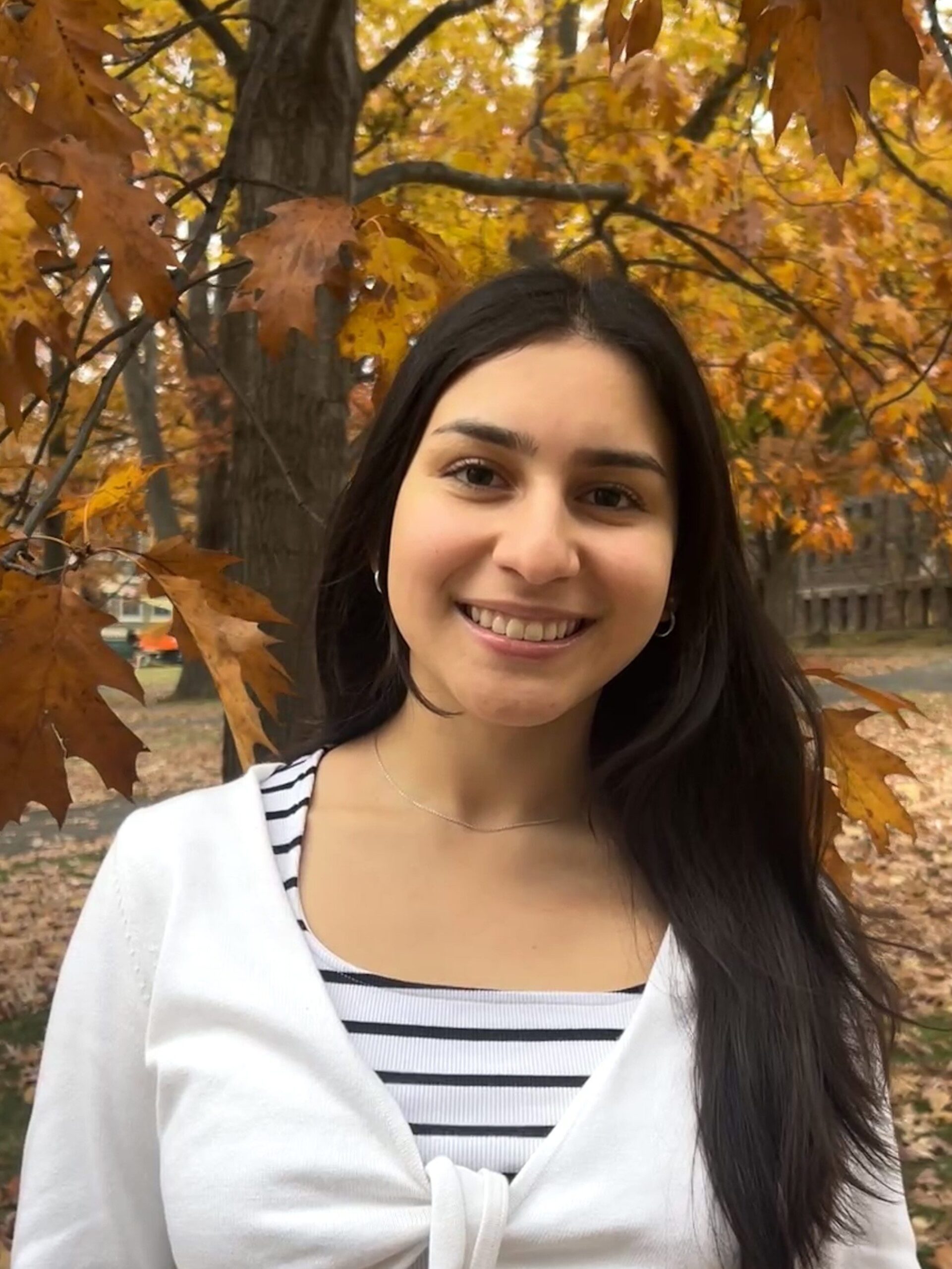 A woman standing in front of fall colors in trees.