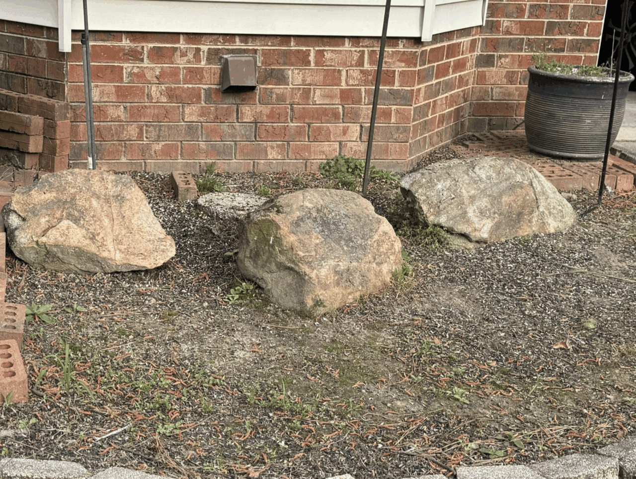 Three large round rocks in a barren space with birdfeeders in the background.