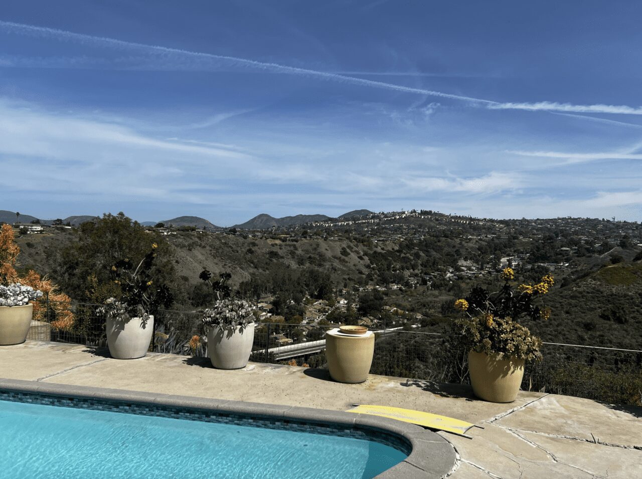 Sunny day in southern California where a pool has five large pots lining it.